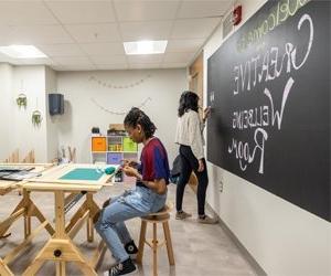 Student drawing on chalkboard and another student using clay at a desk