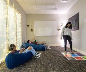 Students sitting on bean bag chairs listening to music and another student interacting with color board on the floor